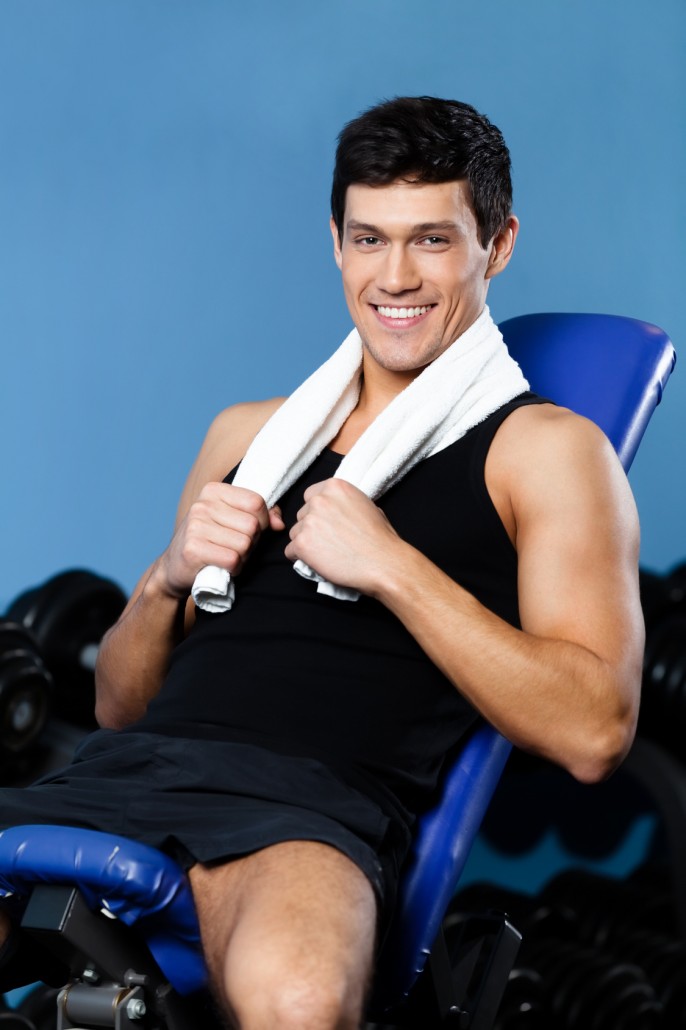 Athletic man rests sitting on blue simulator in training gym